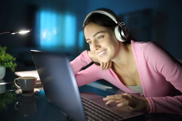 幸せな女性は自宅で夜にノートパソコンやヘッドフォンでメディアを見て — ストック写真