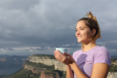 Tatmin olmuş bir kadın kahvesini içiyor bulutlu bir günde yüzünü çeviriyor.