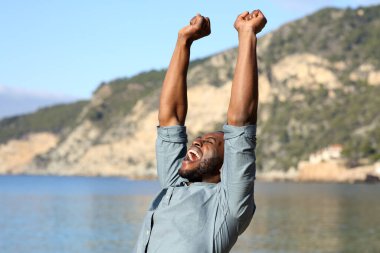 Siyahi tenli, mutlu bir adam plajda tatilini kutluyor.