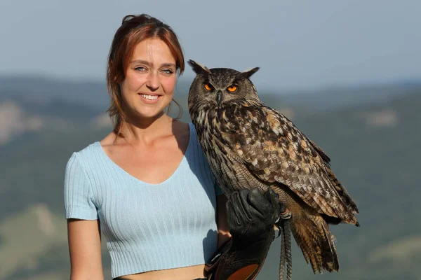 Happy falconer holding a eagle owl looking at you smiling at camera