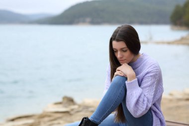 Üzgün genç, bulutlu bir günde gölde otururken aşağıya bakıyor.
