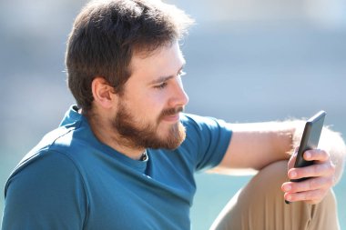 Rahat adam gölde oturmuş cep telefonunu kontrol ediyor.
