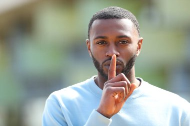 Siyahi tenli bir adamın sokakta sessizlik isteyen portresi.