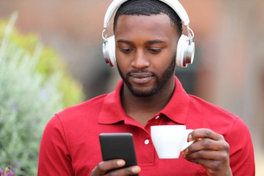 Siyah tenli, kulaklık takan, barda telefonla medyayı izleyen bir adamın portresi.