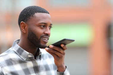 Siyah tenli bir adam sokakta cep telefonunda ses tanıma kullanıyor.