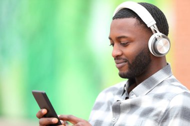 Siyah tenli bir adam müzik dinliyor, cep telefonunu kontrol ediyor.