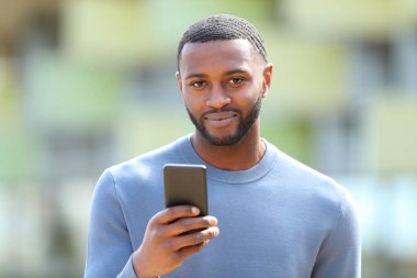 Siyah tenli bir adam sokakta elinde telefonla sana bakıyor.