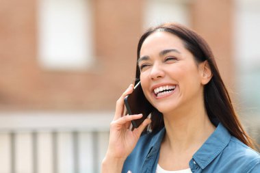 Mutlu bir kadın sokakta telefonla konuşurken gülüyor.