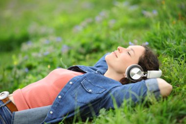 Relaxed woman lying on the grass listening to music with headphones in a park