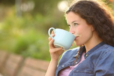 Gün batımında bir bankta oturmuş, kahve içen mutlu bir kadın.