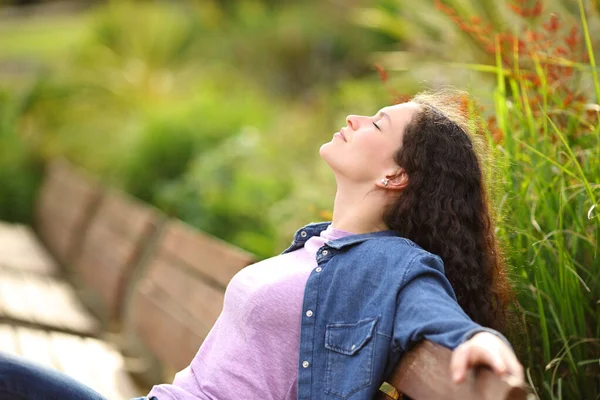 一个女人坐在公园的长椅上放松呼吸新鲜空气的特征 — 图库照片