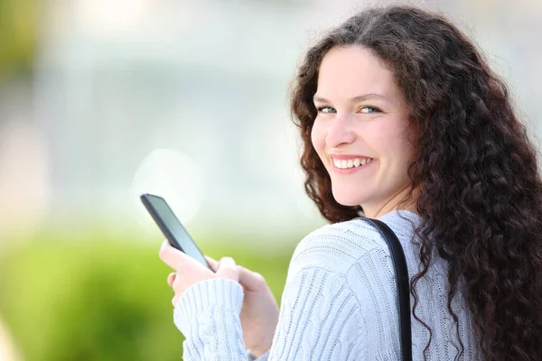 Happy Woman Holding Cell Phone Looks Camera Walking Street — Zdjęcie stockowe