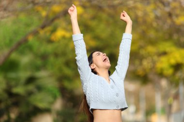 Excited woman raising arms celebrating good day standing in a park 