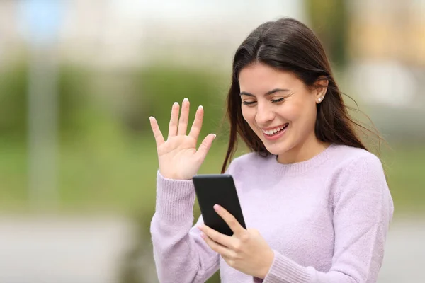 Happy teen greeting during a video call on phone in the street