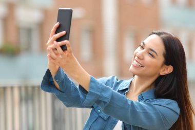 Happy woman posing taking selfie with smart phone in the street