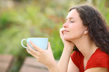 Profile of a relaxed woman resting holding a coffee cup in a park