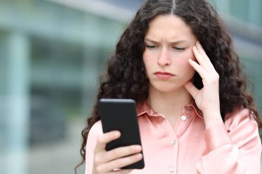 Worried woman reading message on smart phone walking in the street