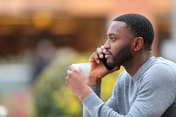 Profile portrait of a man with black skin talking on phone drinking in a coffee shop