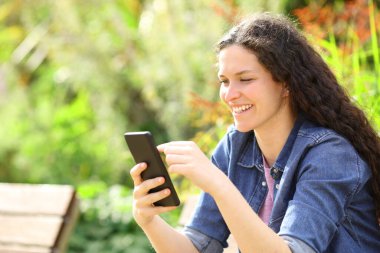 Yeşil bir parkta akıllı telefon kullanan mutlu kadın.