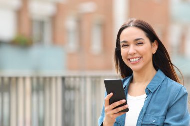Mutlu kadın kameraya bakıyor. Sokakta akıllı telefon tutuyor.