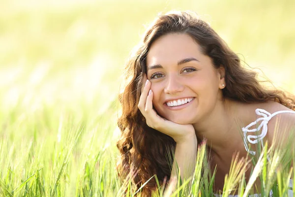 Portrait of a happy woman with perfect smile sitting in a wheat field looking at you