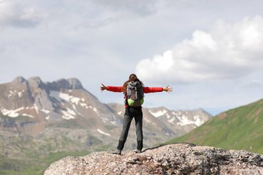 Yürüyüşçü yüksek bir dağın tepesinde kollarını açarak başarıyı kutluyor.
