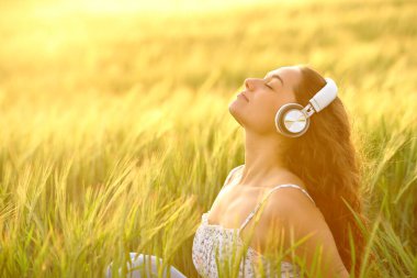 Günbatımında bir tarlada müzik dinleyen rahat bir kadının profili.