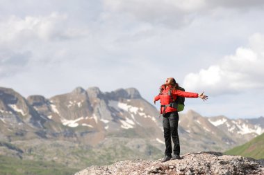 Yüksek bir dağda kollarını açıp çığlık atan heyecanlı bir yürüyüşçü.