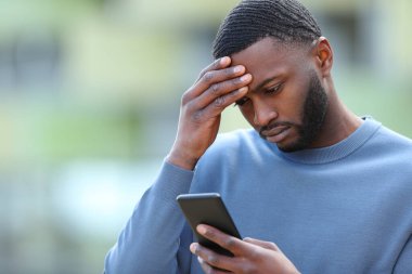 Worried black man checking smart phone in the street