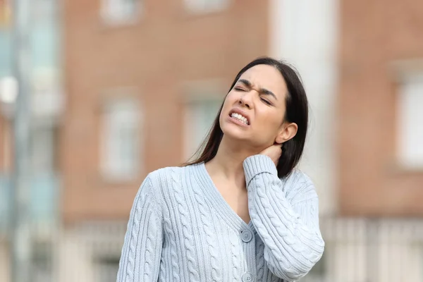 Stressed woman is suffering neck ache complaining alone in the street
