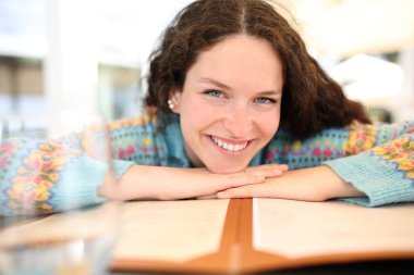 Front view portrait of a happy woman looking at you over a menu card in a bar terrace