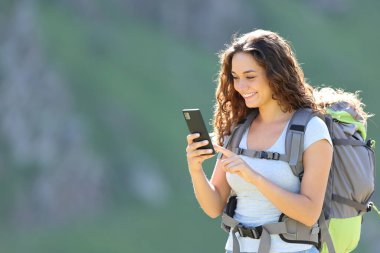 Happy hiker consulting smartphone while trekking in the mountain
