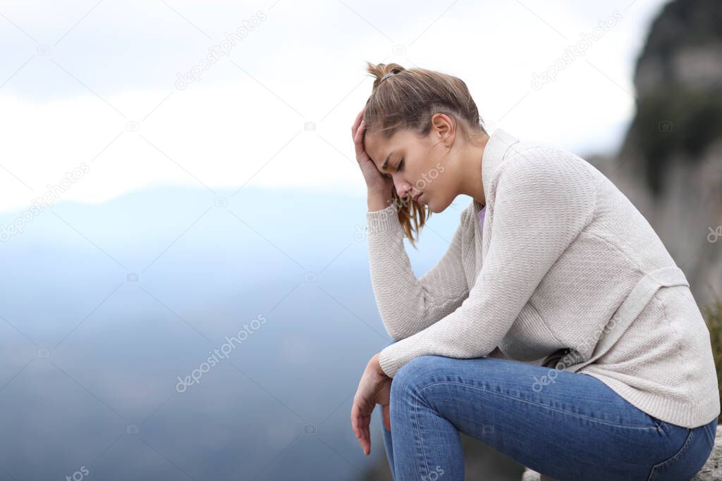Side view portrait of a sad woman complaining alone in the mountain