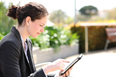 Side view portrait of an executive sitting in a park using tablet