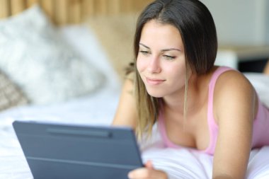 Happy woman using digital tablet lying on a bed at home