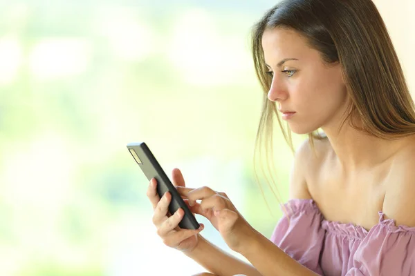 Jovem Mulher Séria Usando Telefone Inteligente Perto Uma Janela Casa — Fotografia de Stock