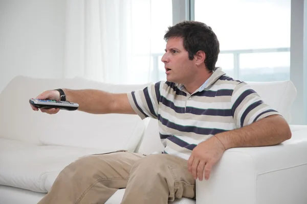 Curious looking man on couch with remote control — Stock Photo, Image