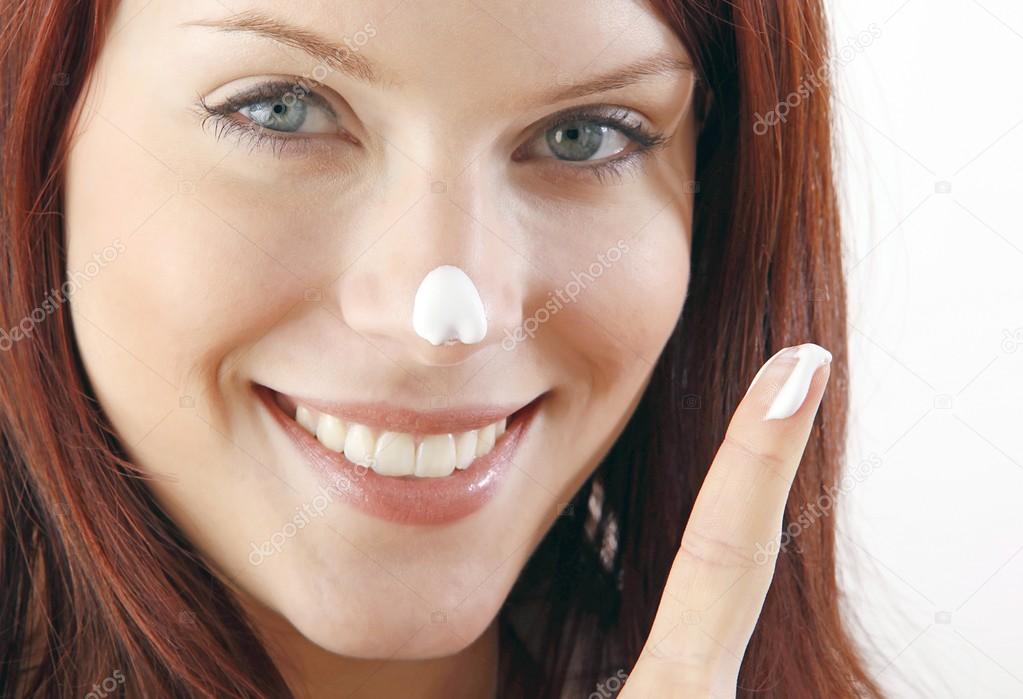Smiling woman put moisturizer cream on nose