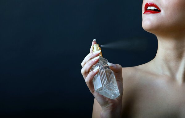 Smiling girl spray the perfume of a bottle