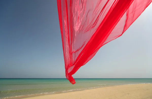 Tecido vermelho se desenvolve no vento na praia — Fotografia de Stock