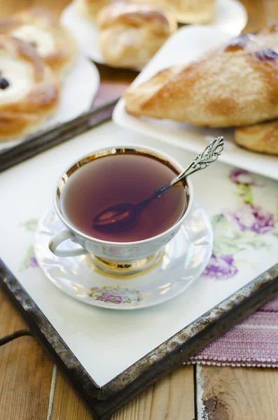 Bułeczki serem i rodzynkami, filiżankę herbaty i kwitnących moreli w wazonie. — Zdjęcie stockowe