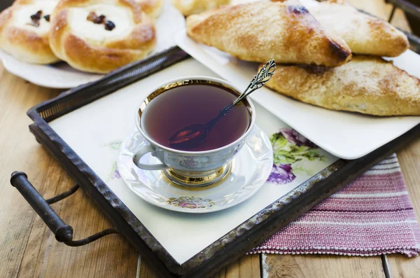 Ost och russin bullar, kopp te och blommande aprikos i vasen. — Stockfoto