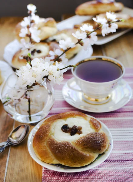 Käse- und Rosinenbrötchen, Tasse Tee und blühende Aprikosen in der Vase. — Stockfoto