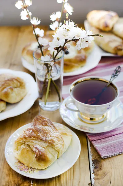 Käse- und Rosinenbrötchen, Tasse Tee und blühende Aprikosen in der Vase. Stockbild