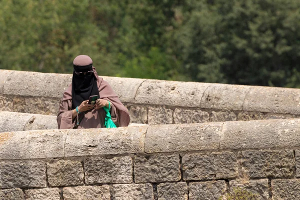 Kobieta Burka Patrząc Telefon Podczas Przekraczania Kamiennego Mostu — Zdjęcie stockowe