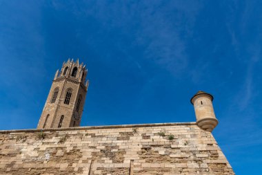 Önünde bir duvar ve sıcak bir yaz gününde açık mavi gökyüzü olan Lleida katedrali kulesi.