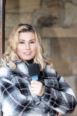 Güzel sarışın gazeteci mikrofona konuşuyor kameraya bakıyor.