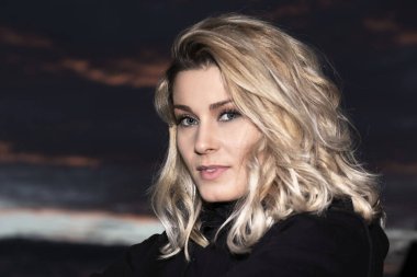 Gün batımında siyah giyinmiş sarışın kadın portresi.