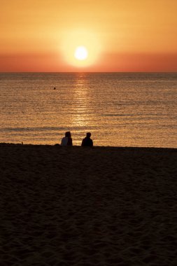 Akdeniz 'deki dostların kumsalında güneşin doğuşunu izleyen çift.