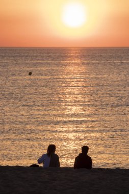 Akdeniz 'deki dostların kumsalında güneşin doğuşunu izleyen çift.